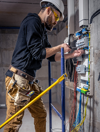 A male electrician works in a switchboard with an electrical connecting cable.